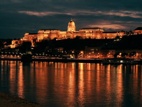 Buda Castle glowing at night, reflecting on the Danube River in Budapest, Hungary.