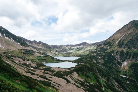 Breathtaking landscape of twin lakes surrounded by Tatra mountains under a cloudy sky.