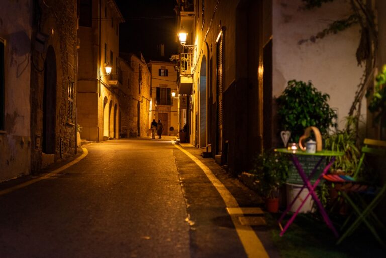 Couple enjoying a romantic evening walk on a charming narrow street in Alcúdia, Spain, lit by warm streetlights.